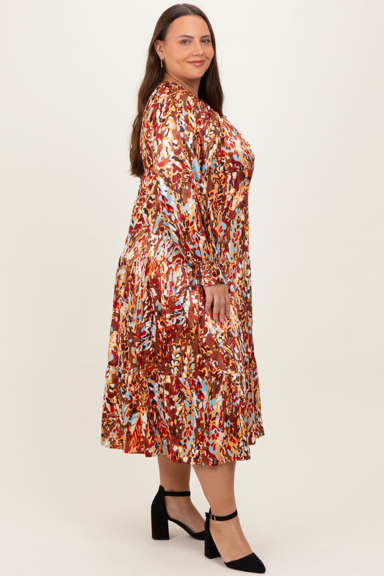 woman wearing a multicolored floral print plus size midi dress with long sleeves and a tiered hem, standing against a neutral background