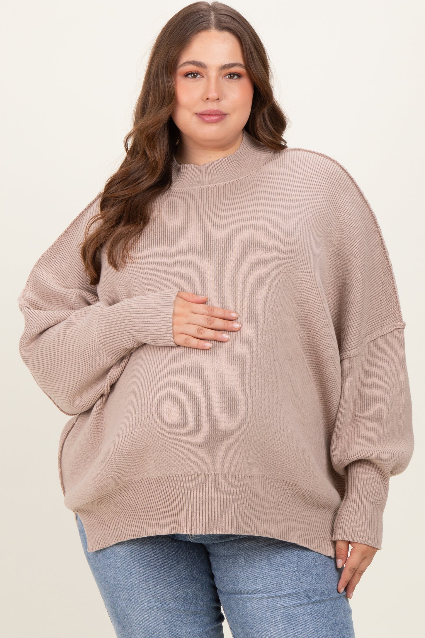 woman wearing a light beige oversized maternity sweater and holding her baby bump