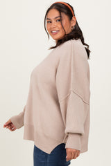 woman wearing a light beige oversized sweater with ribbed details and a high-low hem, paired with blue jeans