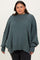 woman wearing a green oversized ribbed sweater with balloon sleeves and a high neckline, paired with black jeans