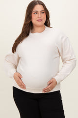 woman wearing a cream oversized maternity sweatshirt and holding her baby bump
