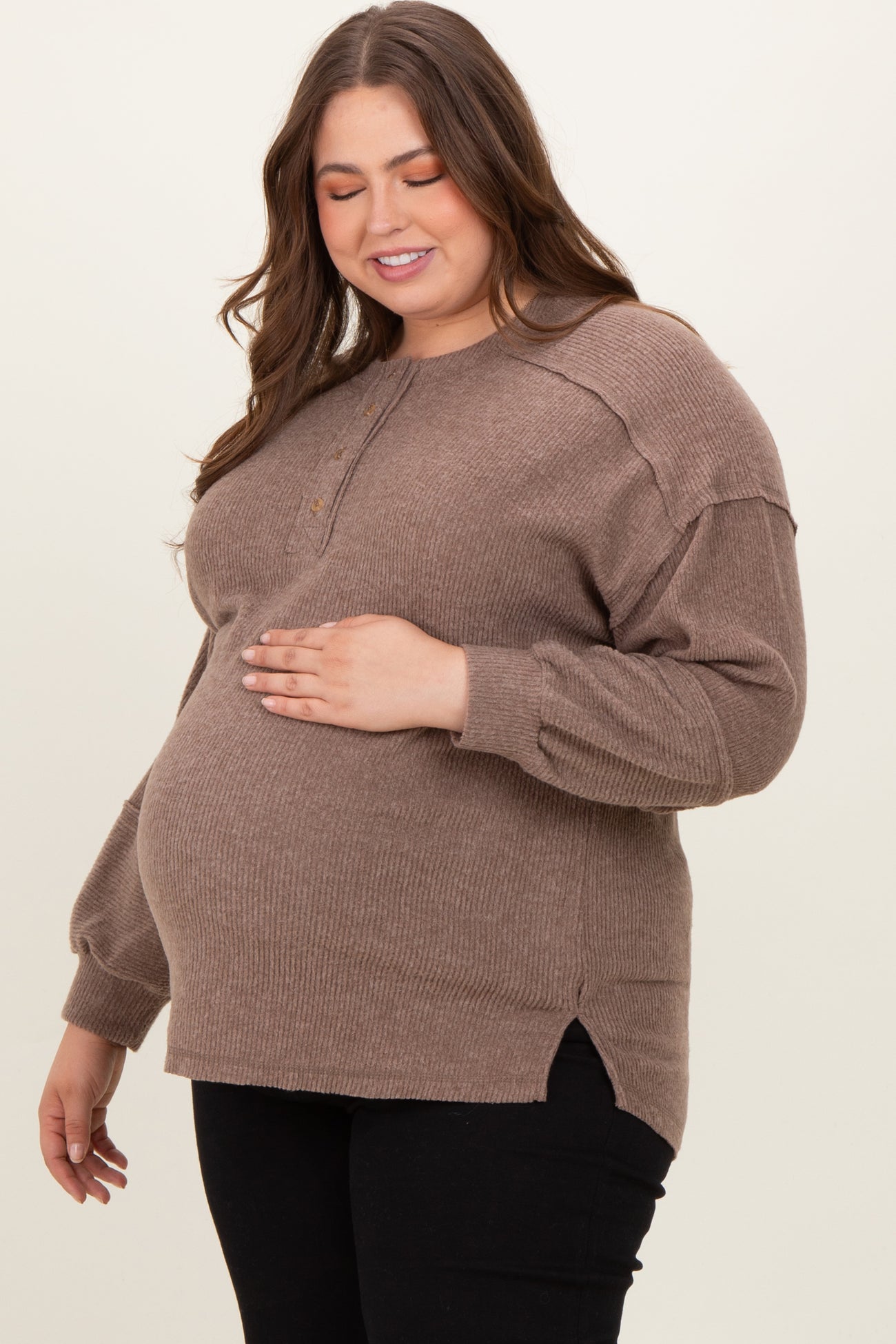 woman wearing a brown ribbed maternity sweater and gently holding her baby bump