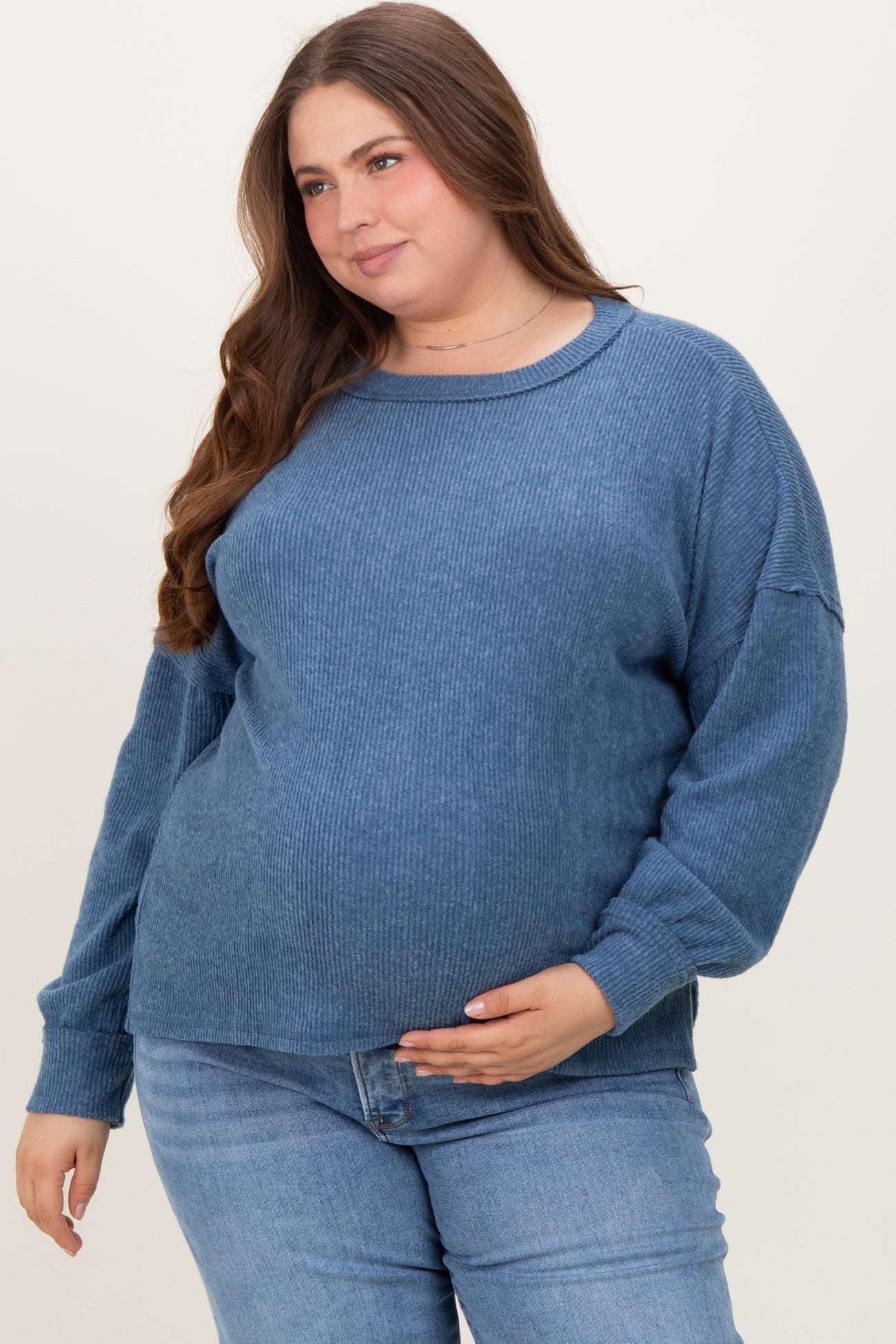 woman wearing a blue ribbed maternity sweater and holding her baby bump