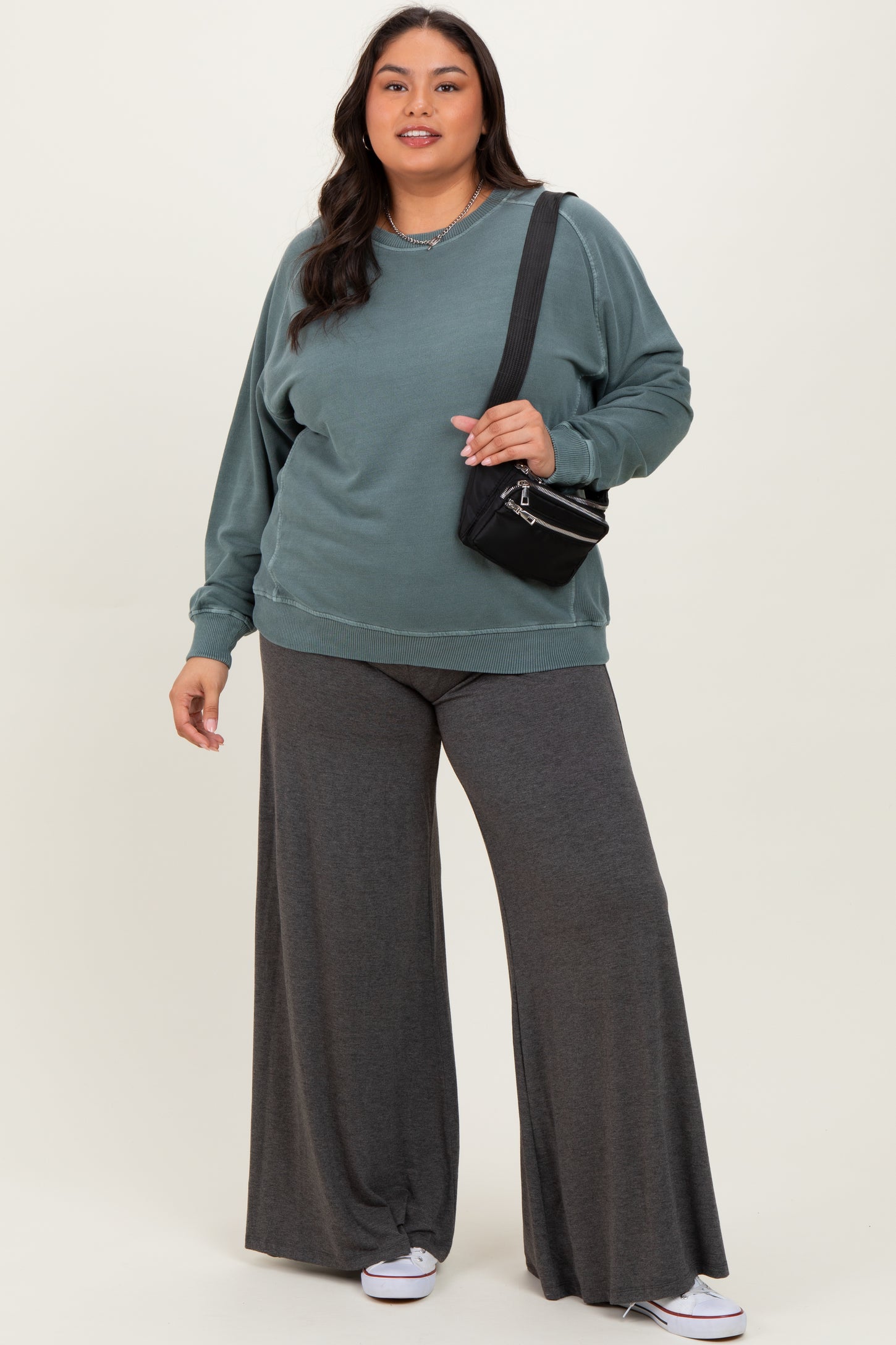 woman wearing a teal oversized sweatshirt and gray wide-leg pants, holding a small black handbag