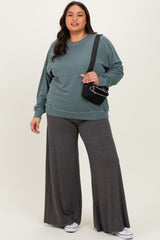 woman wearing a teal oversized sweatshirt and gray wide-leg pants, holding a small black handbag
