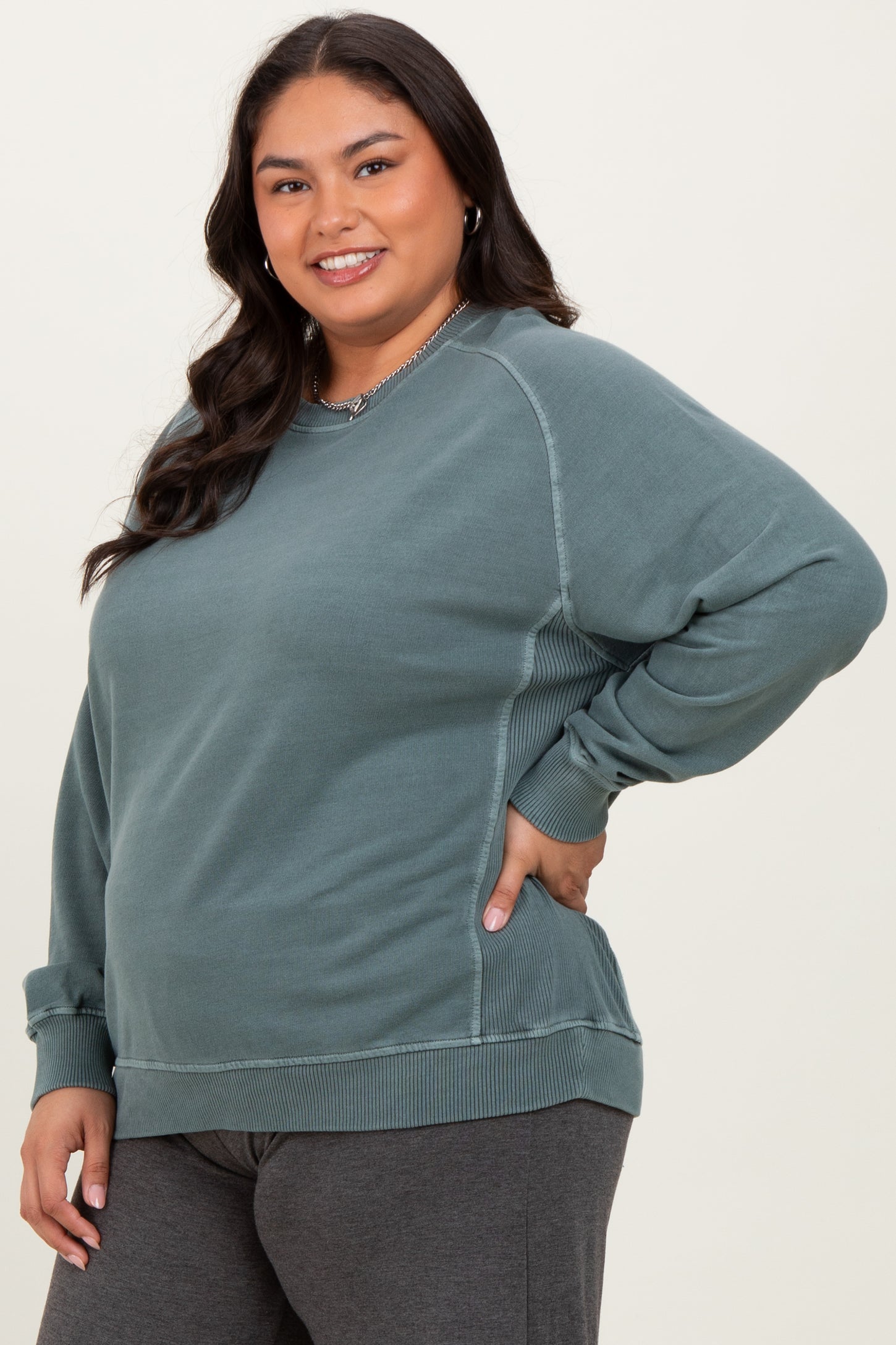 woman wearing a teal plus-size sweatshirt with side panel details and a relaxed fit, smiling at the camera