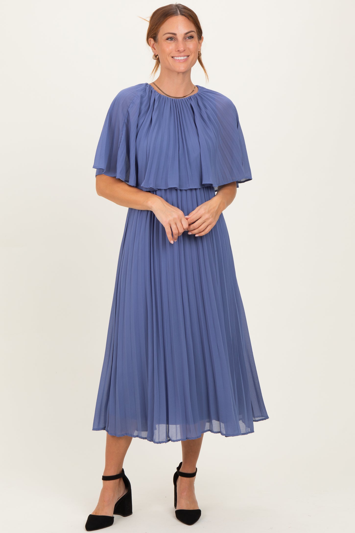 woman wearing a pleated midi dress in soft blue with a cape-style overlay and elegant black heels