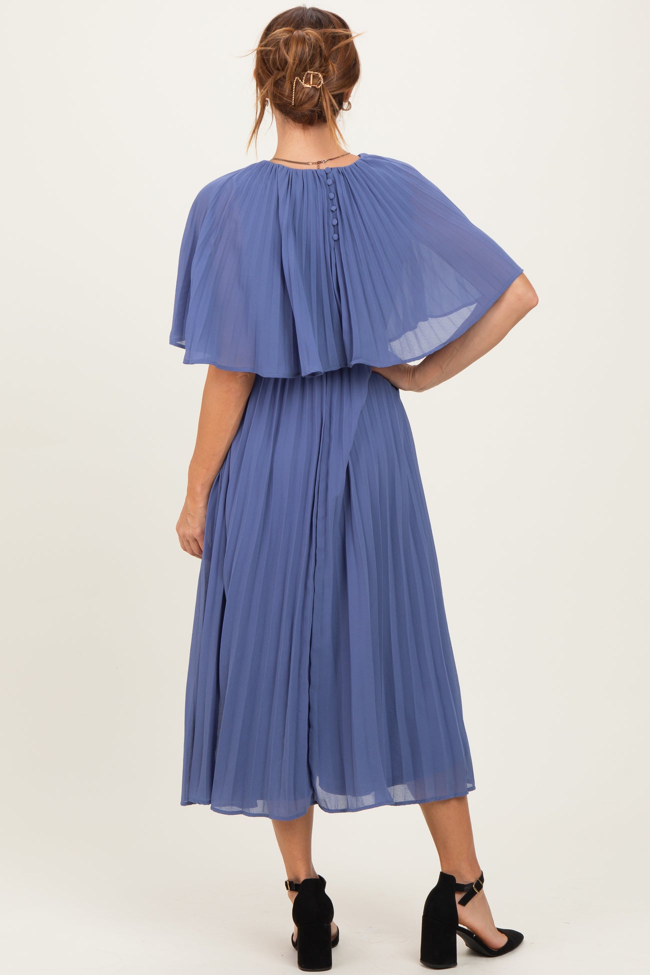 woman wearing a pleated blue midi dress with cape sleeves and button details at the back