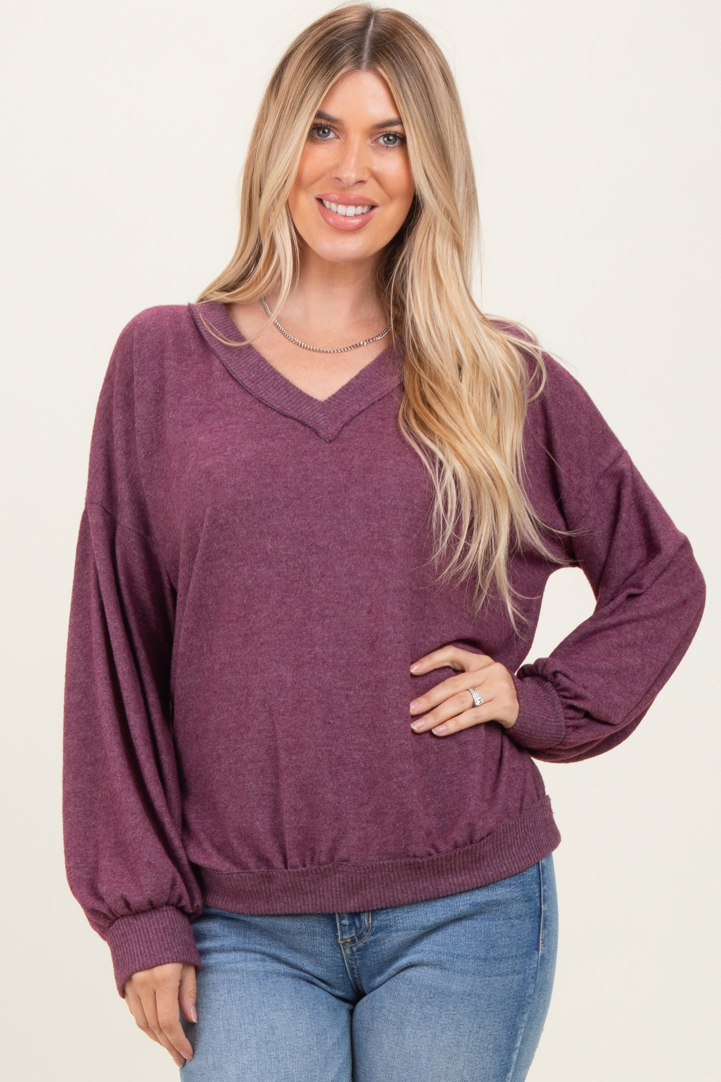 woman wearing a burgundy v-neck oversized sweater with balloon sleeves and a fitted waist, paired with light blue jeans