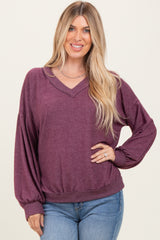 woman wearing a burgundy v-neck oversized sweater with balloon sleeves and a fitted waist, paired with light blue jeans