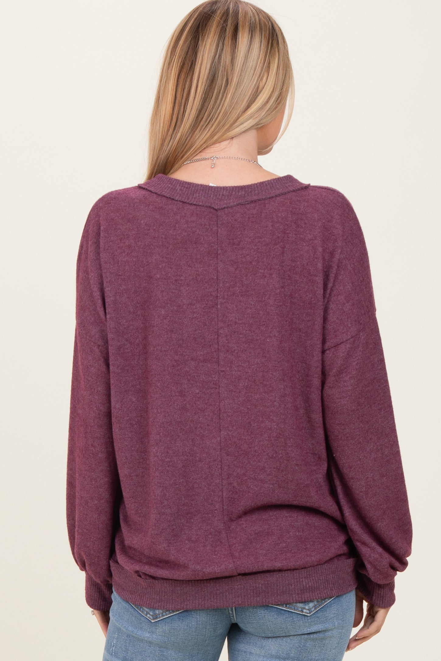 woman wearing a maroon oversized sweater with a relaxed fit, viewed from the back, paired with light blue jeans