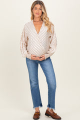 woman wearing a beige polka dot maternity wrap top and holding her baby bump paired with blue jeans