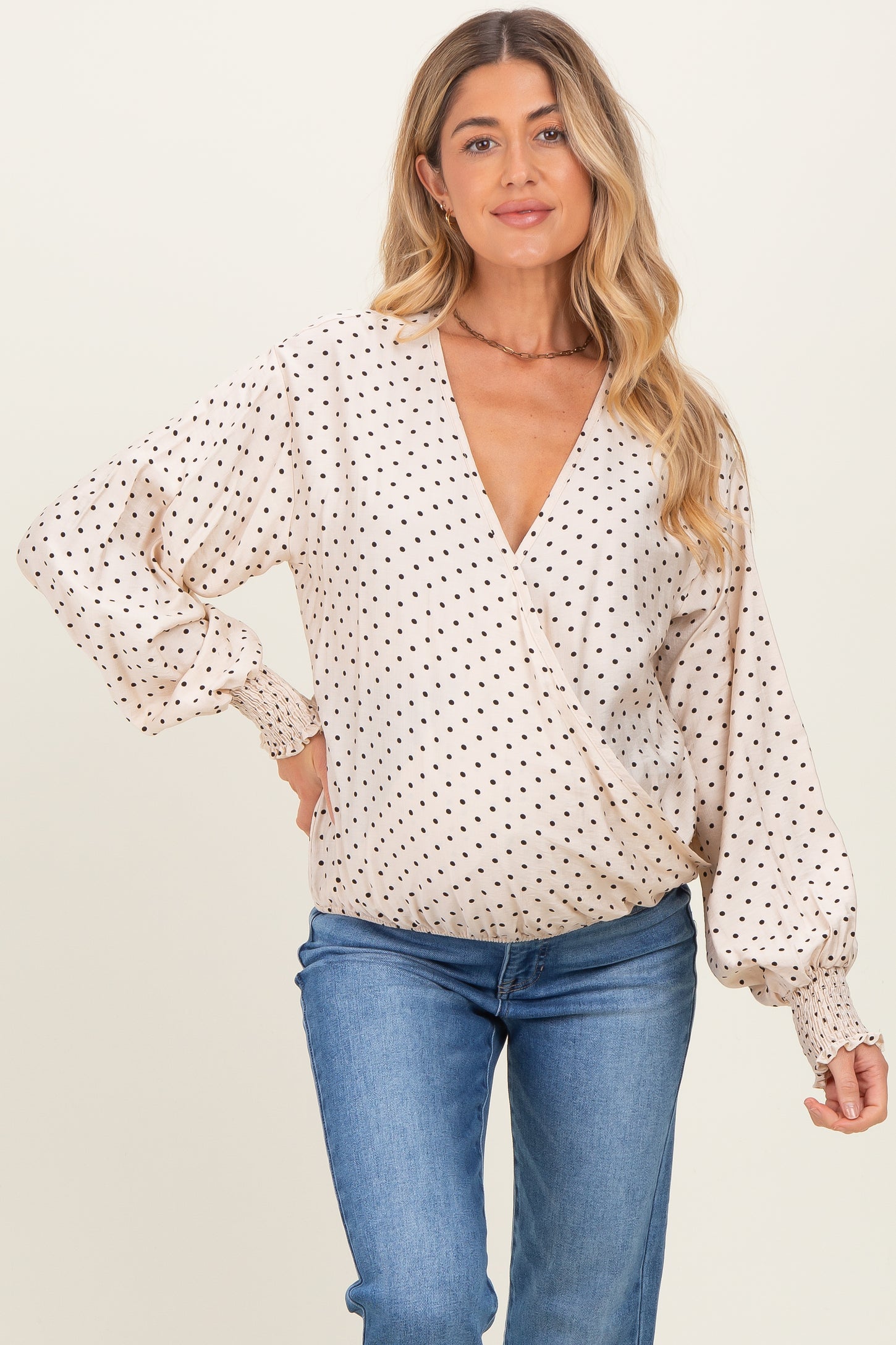 woman wearing a beige maternity wrap top with black polka dots and puffy sleeves, paired with blue jeans