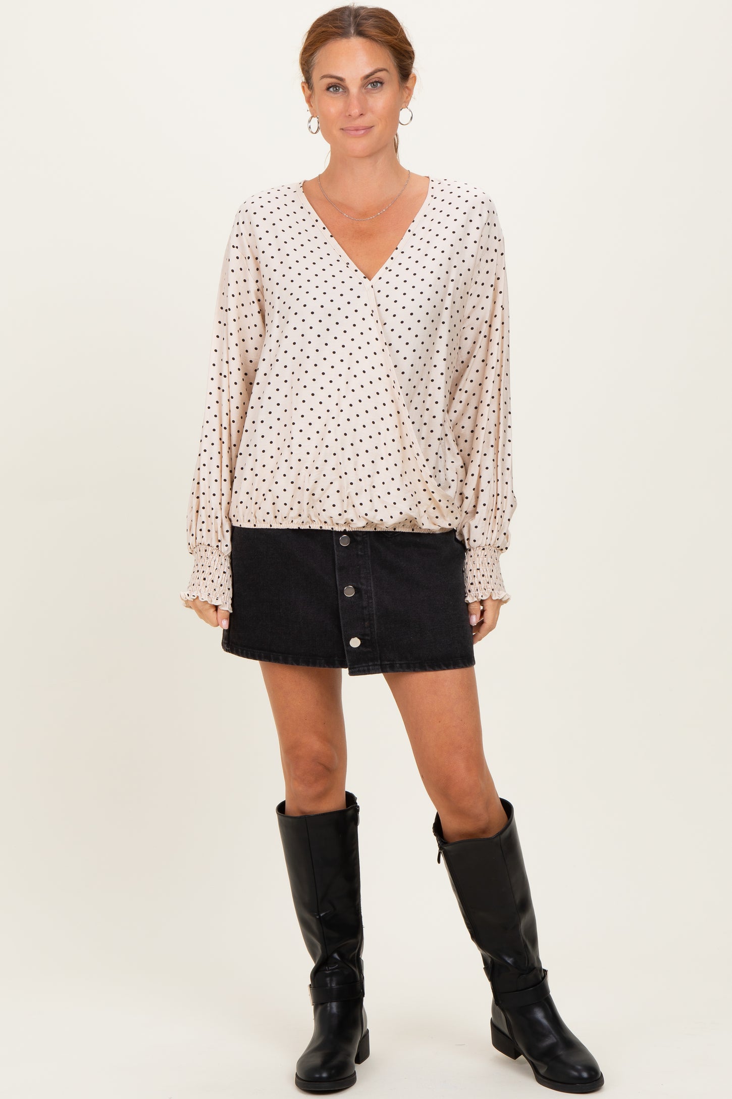 woman wearing a cream polka dot wrap blouse with long sleeves and a black denim button skirt, paired with knee-high black boots