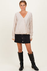 woman wearing a cream polka dot wrap blouse with long sleeves and a black denim button skirt, paired with knee-high black boots