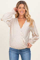 woman wearing a beige maternity wrap top with black polka dots and balloon sleeves, styled with blue jeans