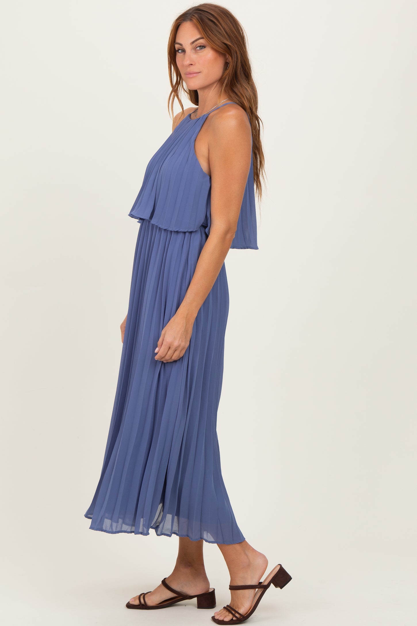 woman wearing a sleeveless lavender pleated maxi dress with layered bodice and strappy sandals