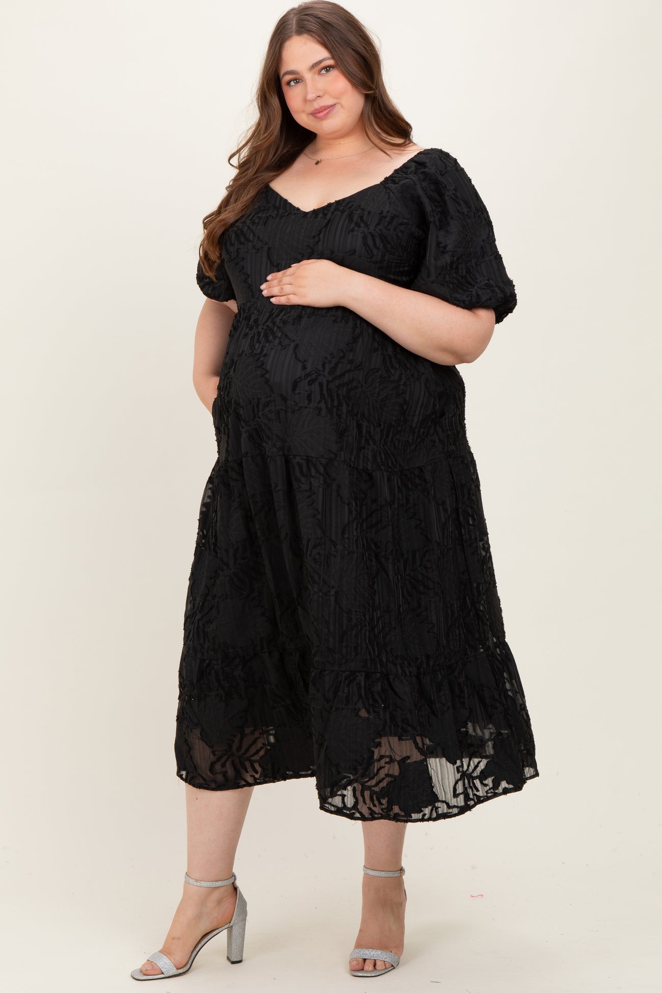 woman wearing a black maternity plus dress with floral detailing, cradling her baby bump