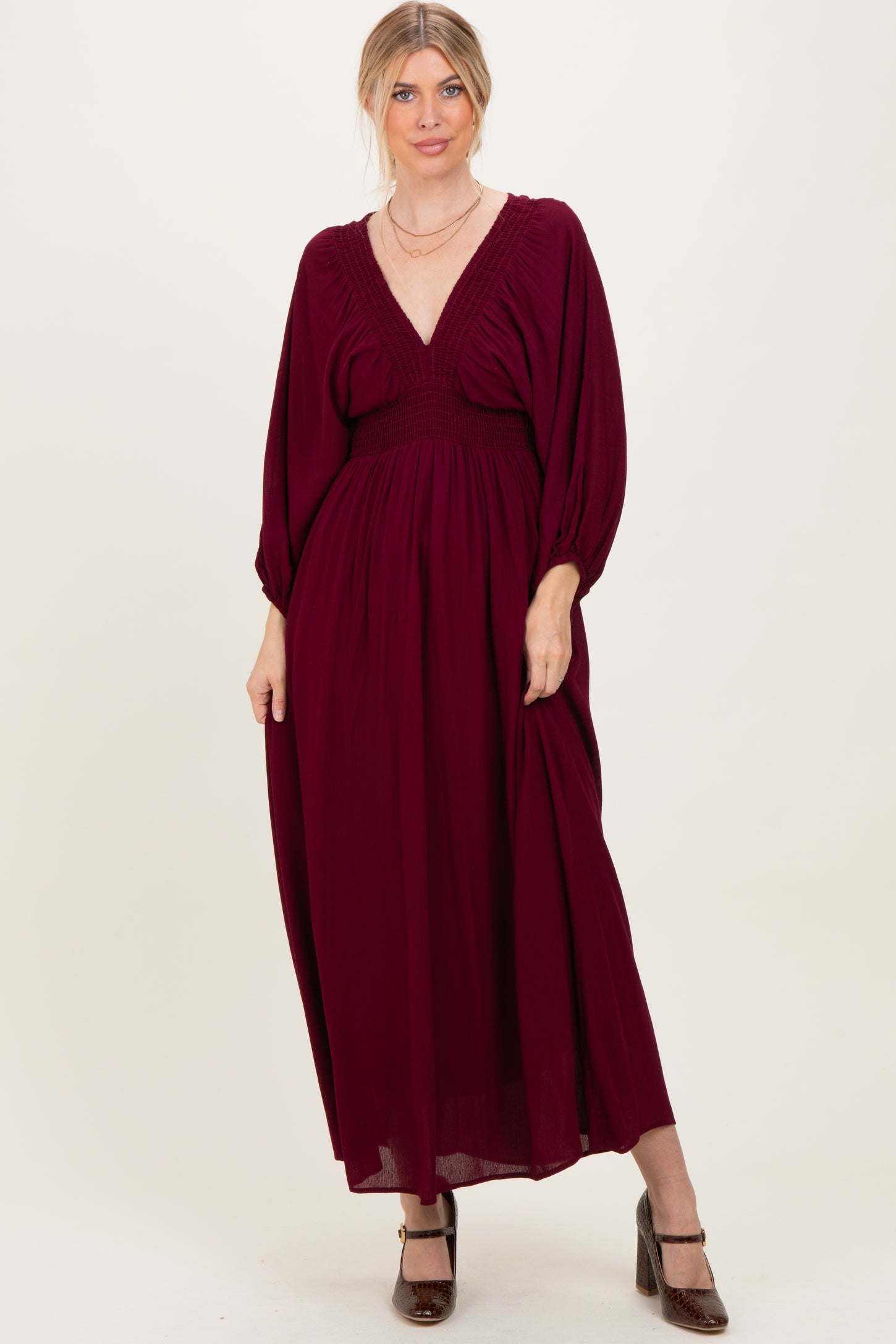 woman wearing a burgundy maxi dress with a deep v-neck and smocked bodice, styled with a flowy skirt and balloon sleeves