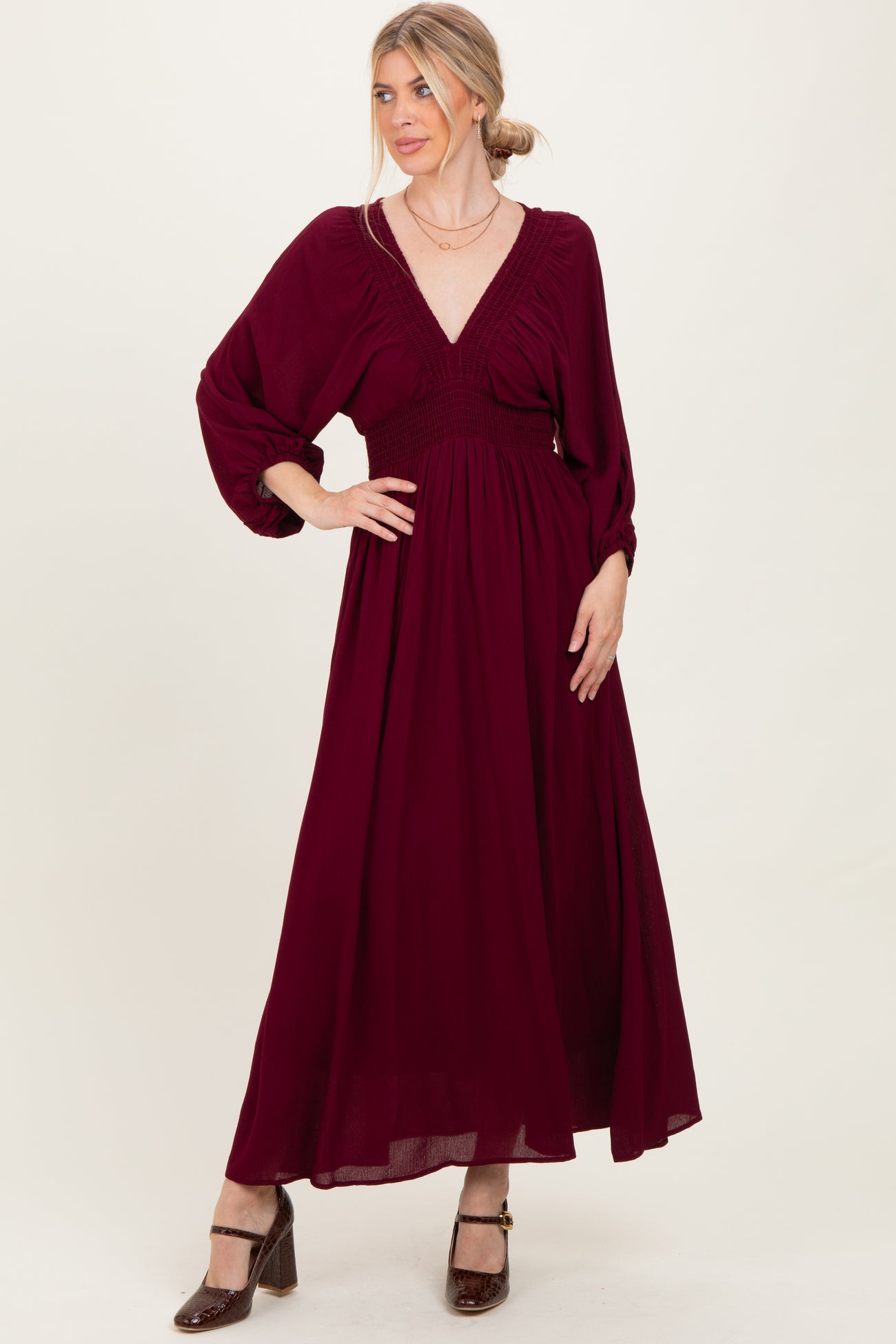 woman wearing a burgundy long sleeve maxi dress with a deep v-neck and smocked waist, styled with heels