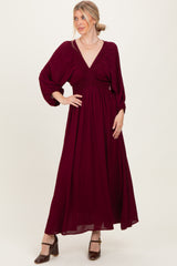 woman wearing a burgundy long sleeve maxi dress with a deep v-neck and smocked waist, styled with heels