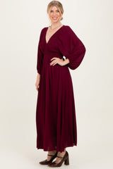 woman wearing a burgundy maxi dress with v-neckline and puff sleeves, standing with a smile