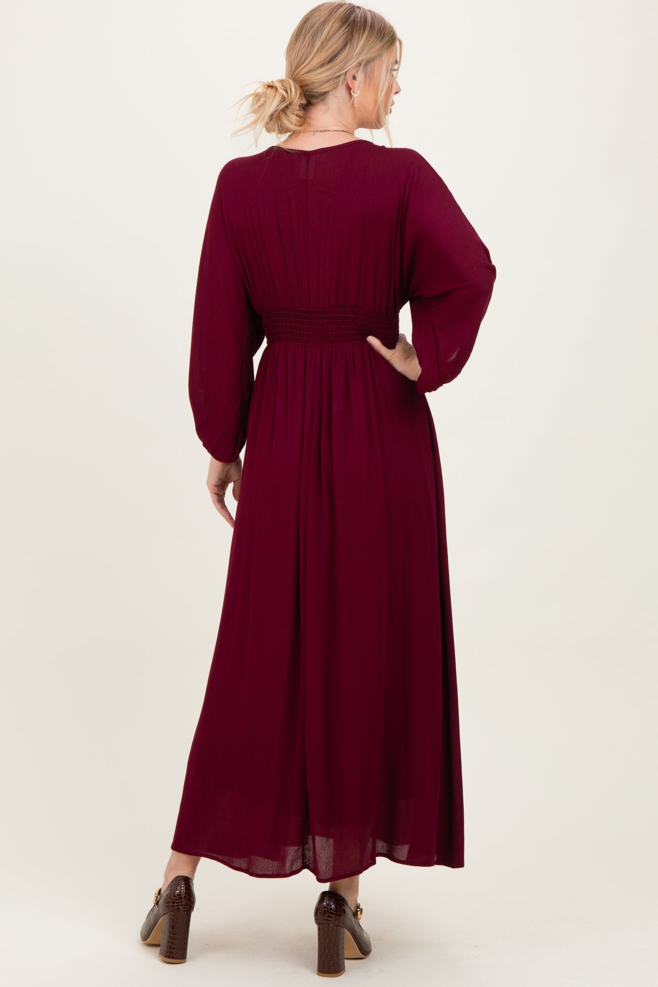 woman wearing a burgundy long sleeve maxi dress with a smocked waist and flowing skirt, shown from the back
