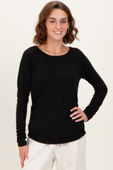 woman wearing a black long sleeve top with ruched details, smiling against a neutral background