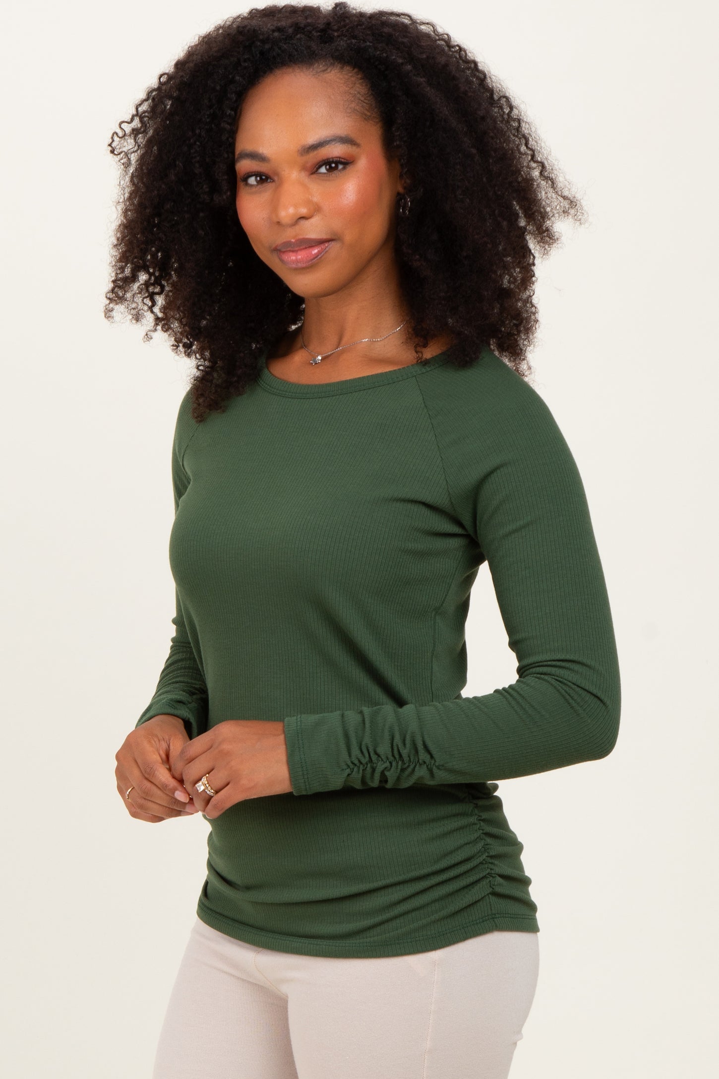 woman wearing a green long sleeve top with ruched sides and a round neckline