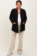 woman wearing a black open front maternity cardigan with pockets over a white top and beige maternity pants, showing her baby bump