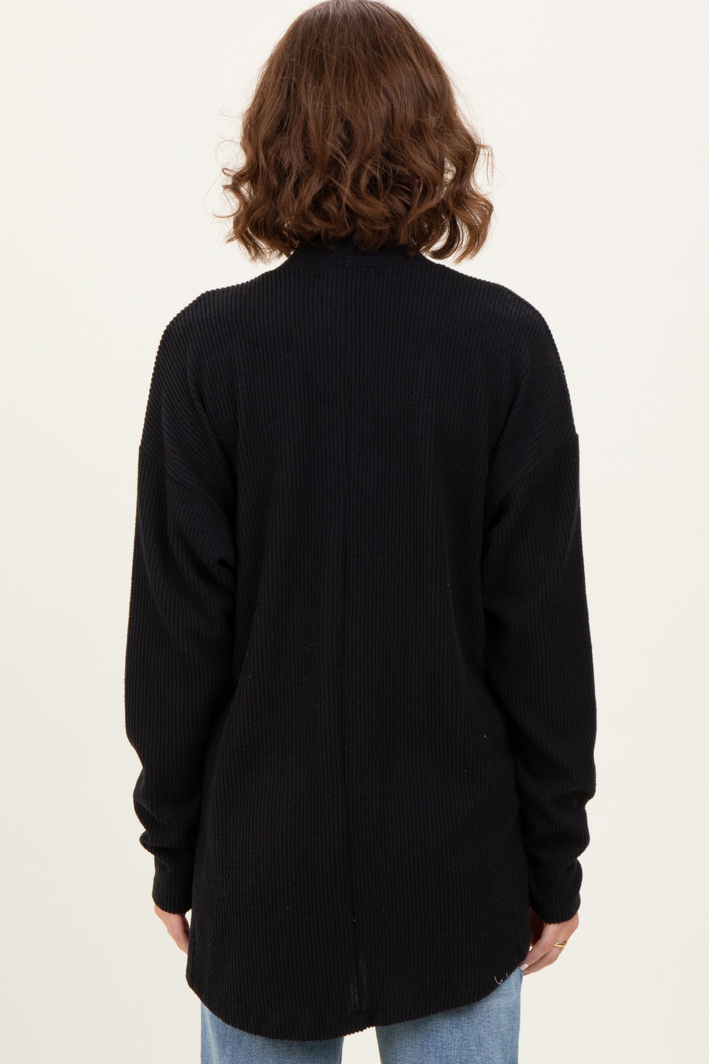 woman wearing a black oversized ribbed sweater with a long back and loose fit, viewed from the back