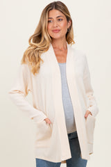 woman wearing a light beige maternity cardigan over a gray top and showing her baby bump, with pockets and relaxed fit