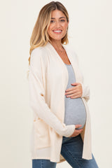 woman wearing a beige ribbed maternity cardigan over a gray top and holding her baby bump