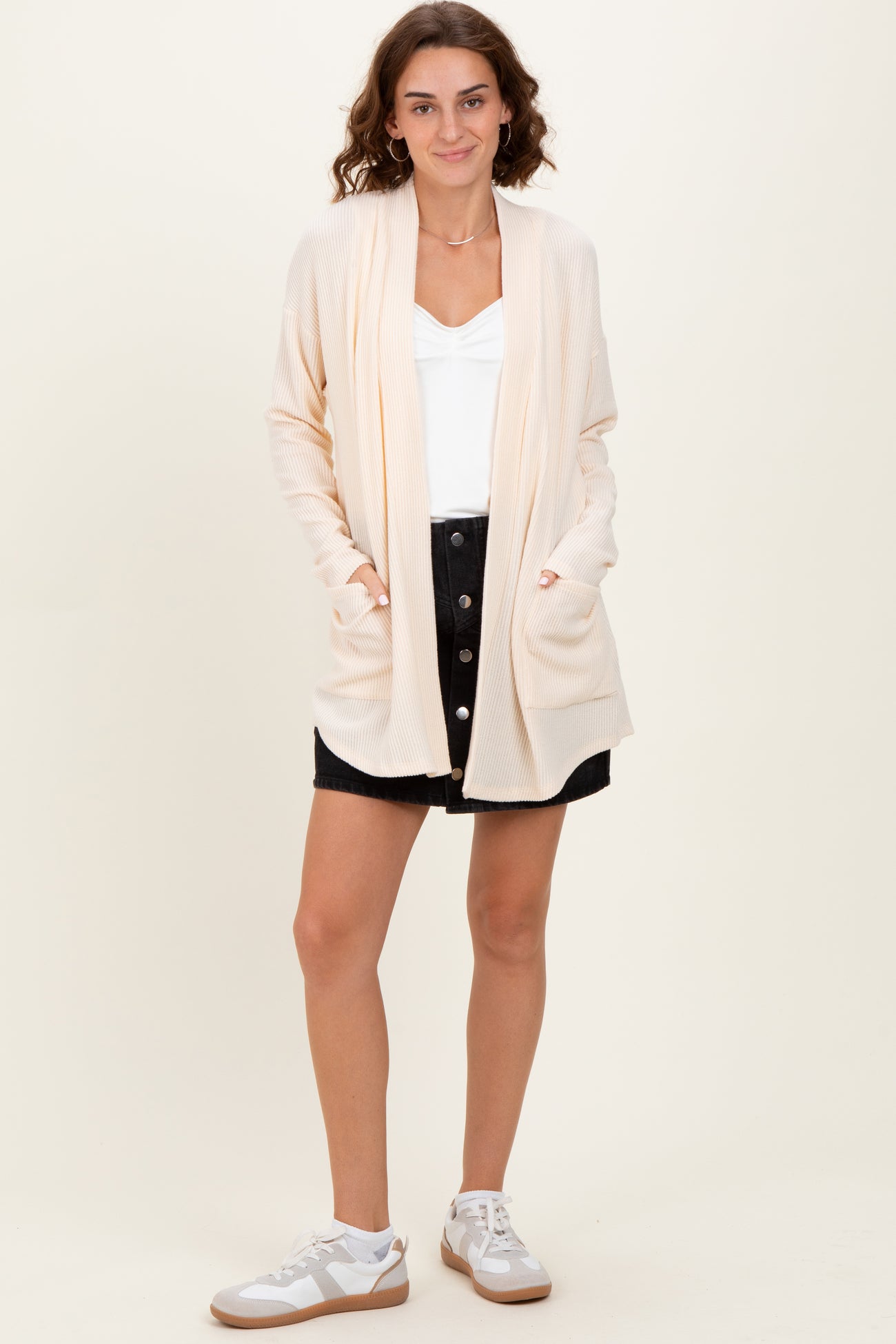 woman wearing a beige open front cardigan over a white top and black button-down skirt with white sneakers