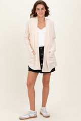 woman wearing a beige open front cardigan over a white top and black button-down skirt with white sneakers