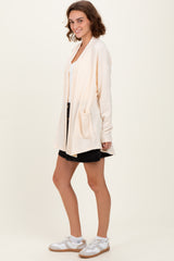 woman wearing a light beige long sleeve cardigan with front pockets, paired with a black skirt and white sneakers