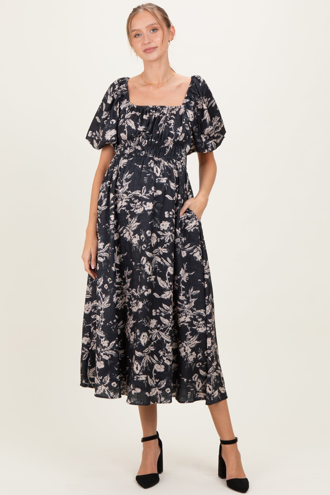 woman wearing a black floral maternity dress with puff sleeves and pockets, displaying her baby bump