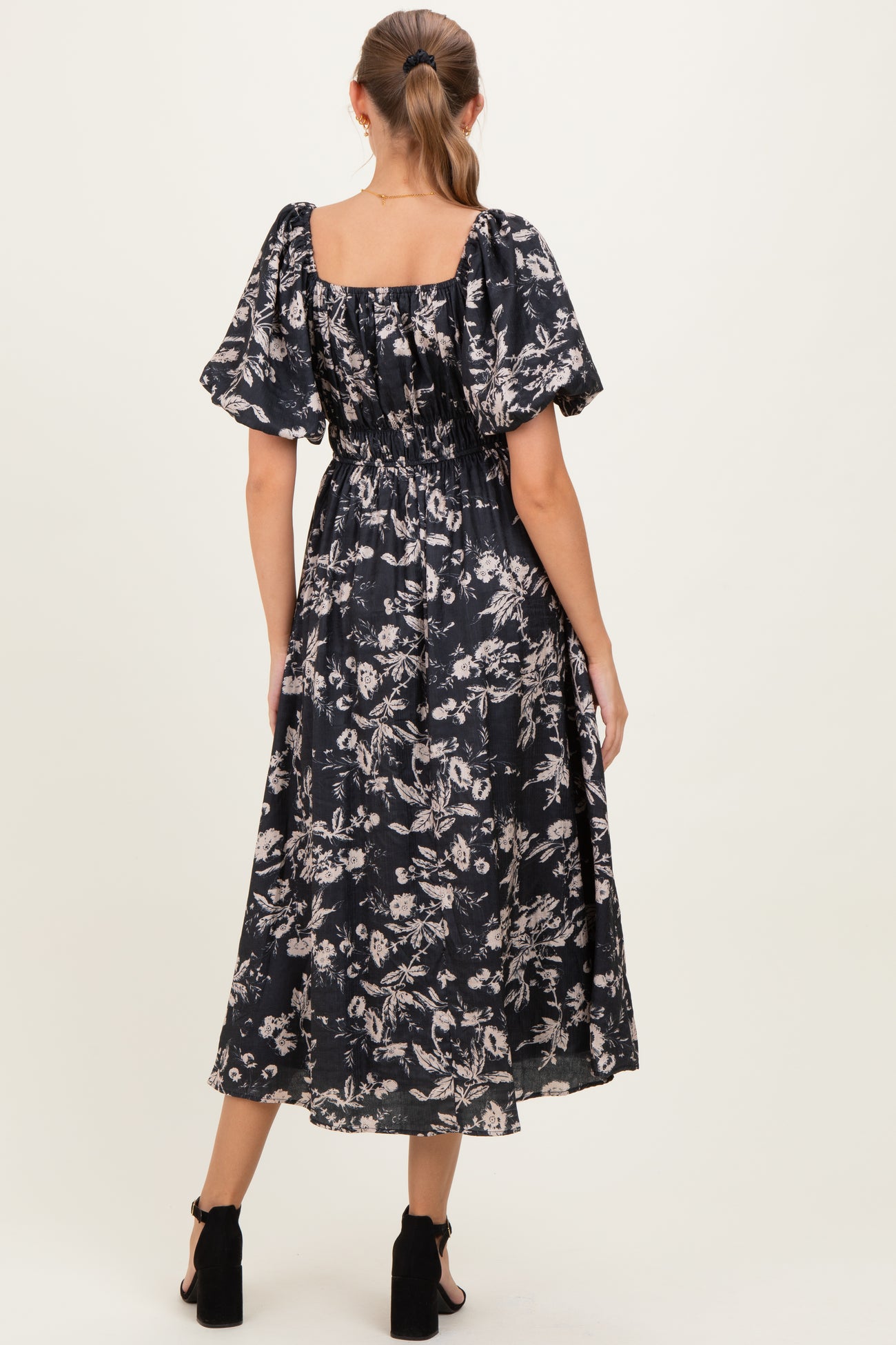 woman wearing a black floral maternity maxi dress with short puff sleeves and a cinched waist, showing her baby bump