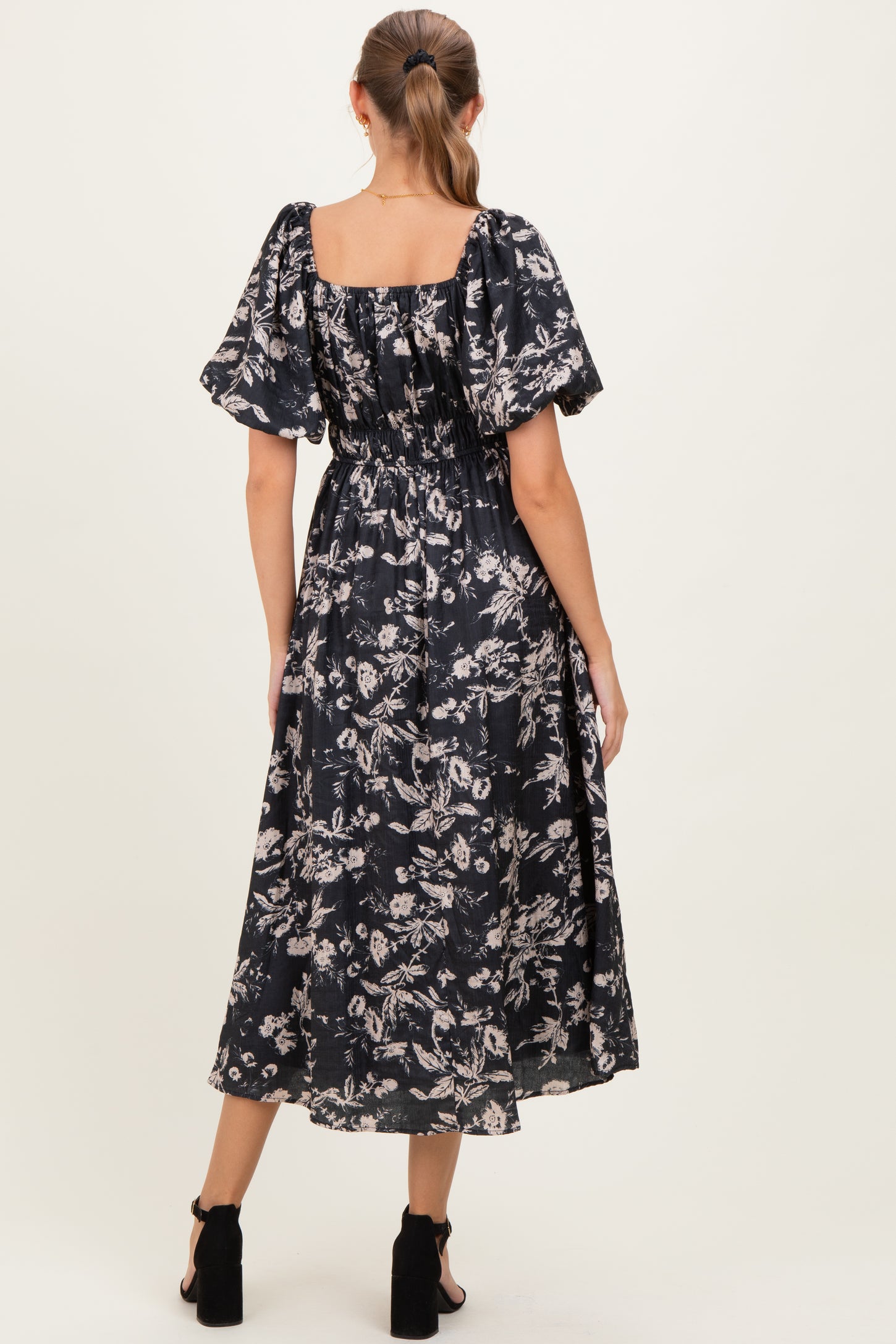 woman wearing a black floral maternity maxi dress with short puff sleeves and a cinched waist, showing her baby bump