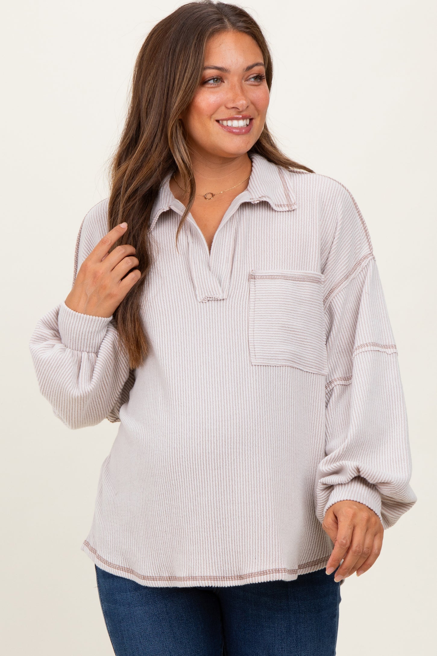 woman wearing a light pink maternity pullover with a collared neckline and pocket, showing her baby bump