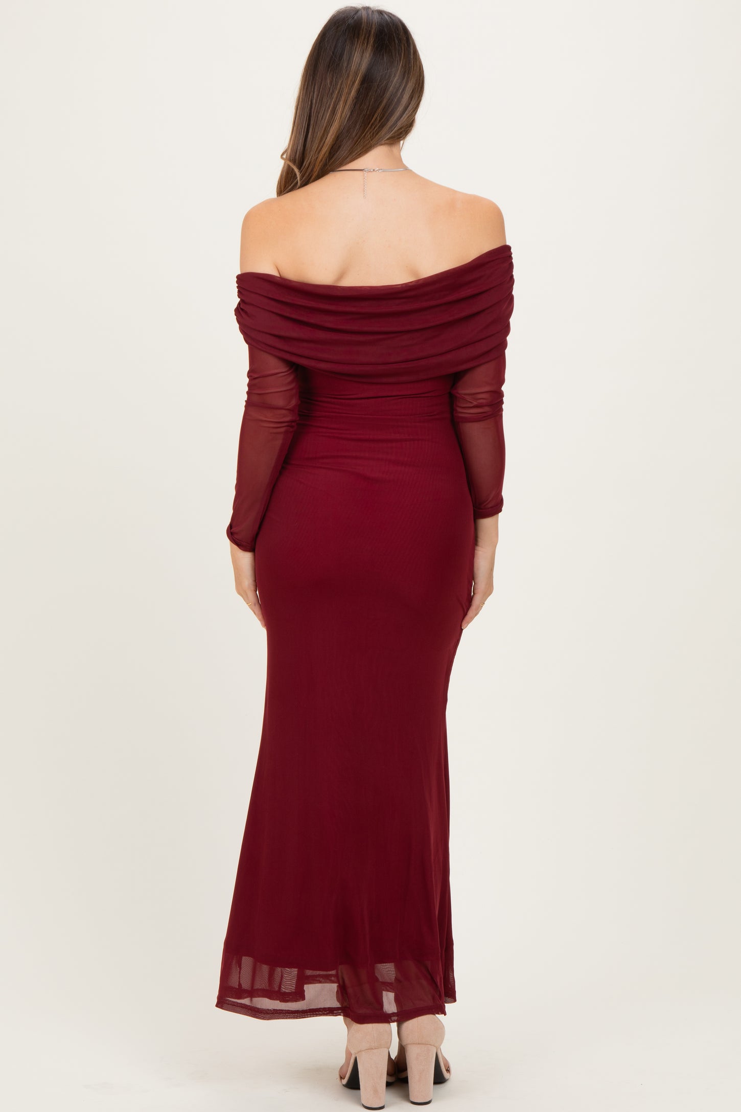 woman wearing a burgundy off-the-shoulder maternity dress with long sleeves and a flowy skirt, showing her back