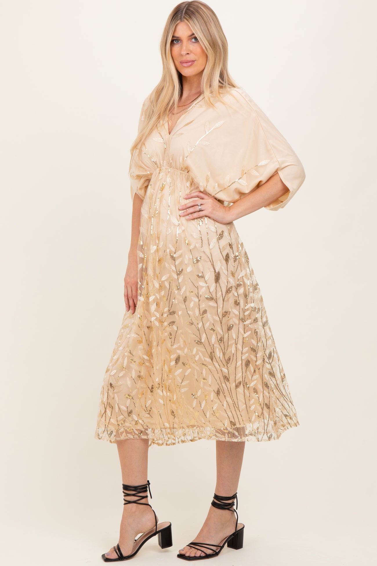 woman wearing a beige midi dress with floral embroidery and short sleeves, standing in stylish black heeled sandals