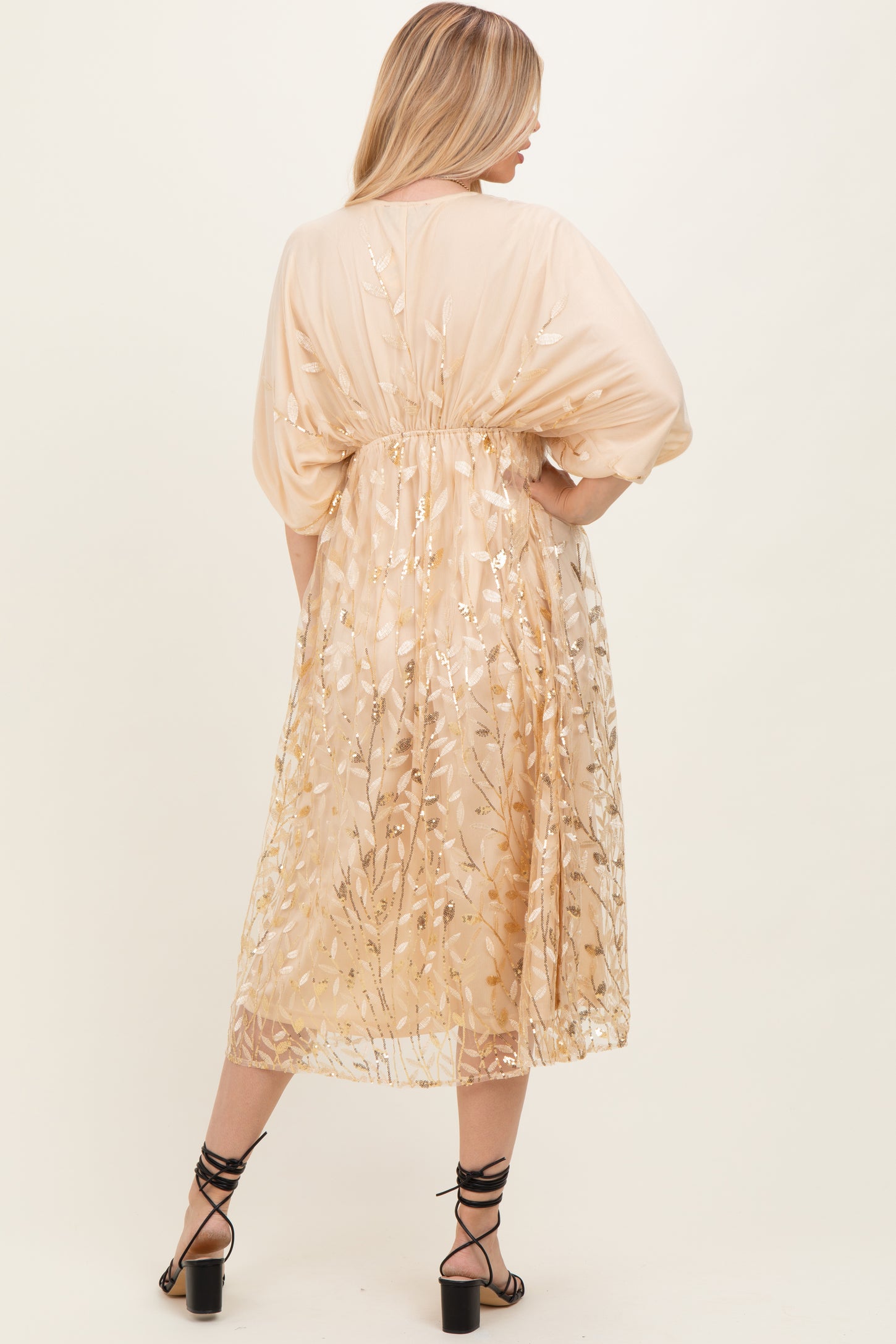 woman wearing a beige floral embroidered maxi dress with a flowy silhouette and tied waist, shown from the back