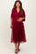 woman wearing a burgundy maternity dress with floral embroidery and a flowy overlay, holding her baby bump