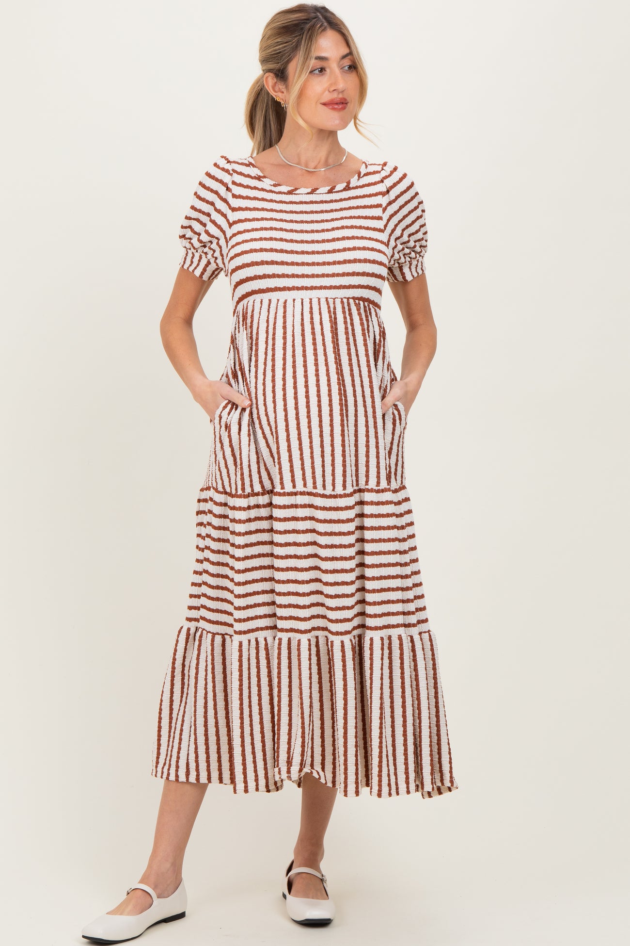 woman wearing a brown and white striped maternity maxi dress with short puff sleeves and pockets