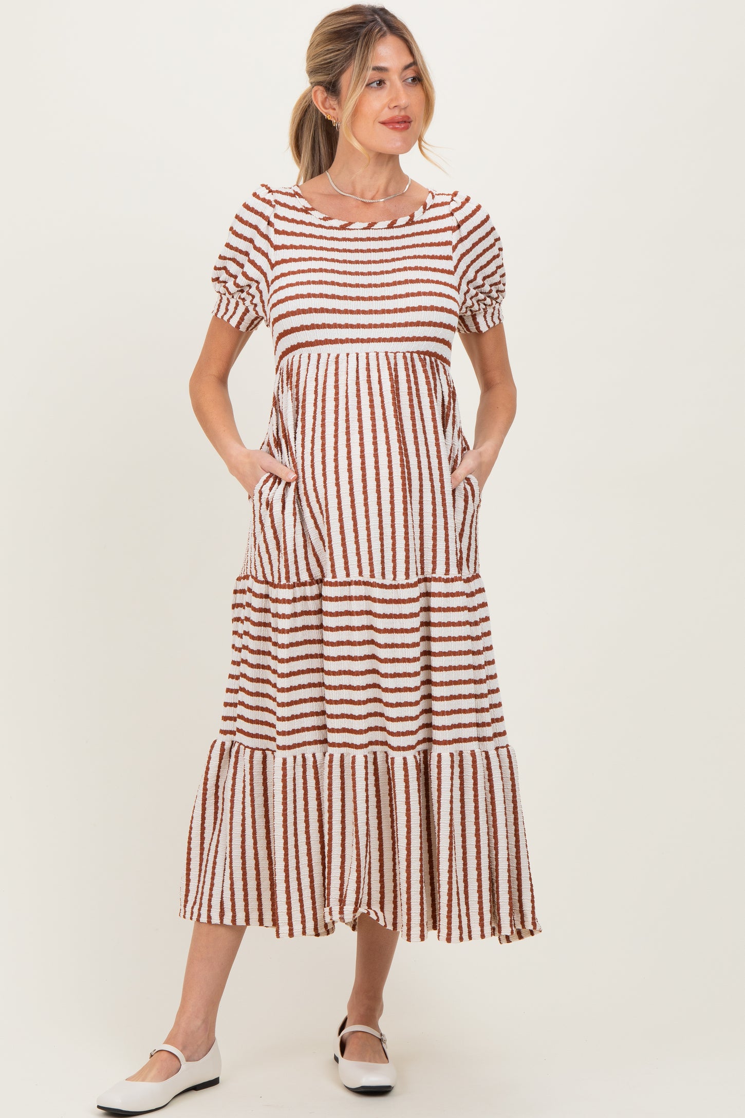 woman wearing a brown and white striped maternity maxi dress with short puff sleeves and pockets