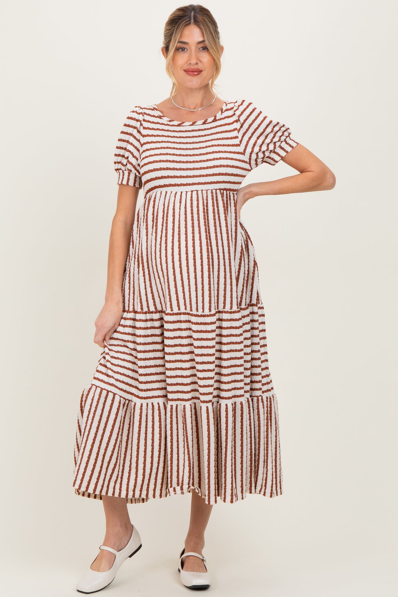woman wearing a brown and white striped maternity maxi dress with short sleeves and a tiered skirt, showing her baby bump