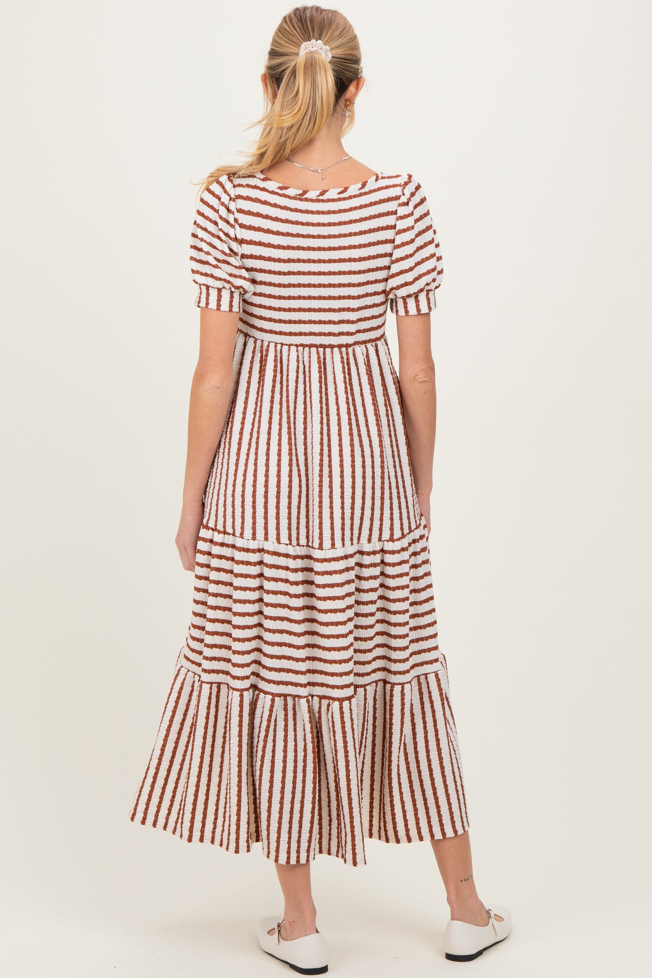 woman wearing a striped maternity dress with short puff sleeves and a tiered skirt, showing the back view