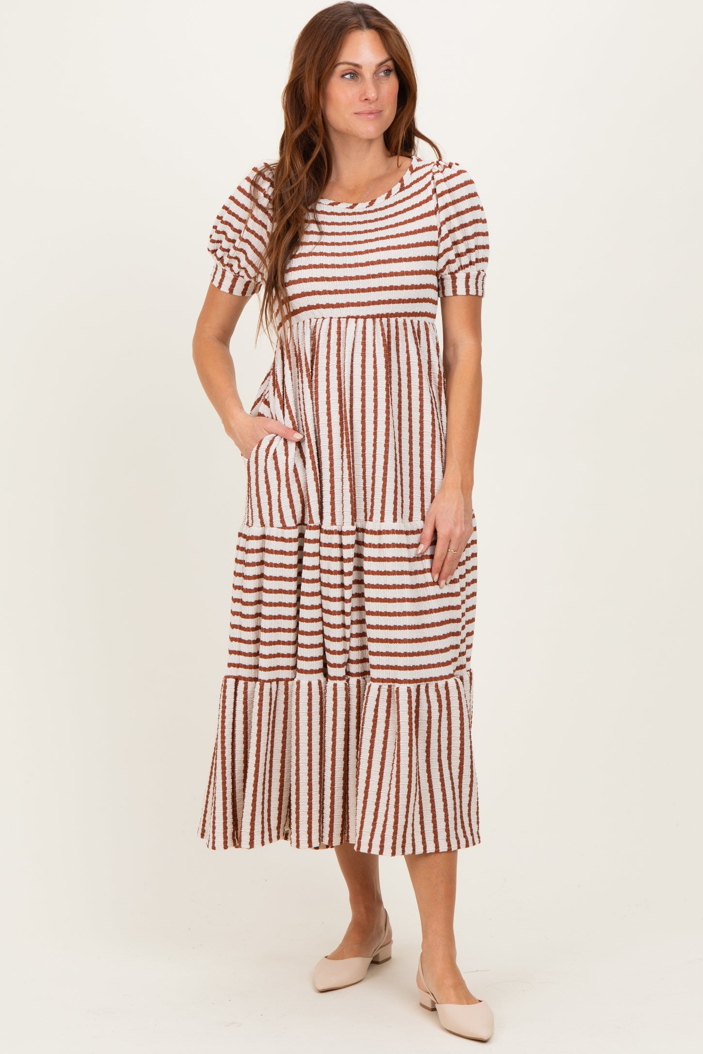 woman wearing a striped tiered midi dress with puff sleeves and pockets in neutral tones