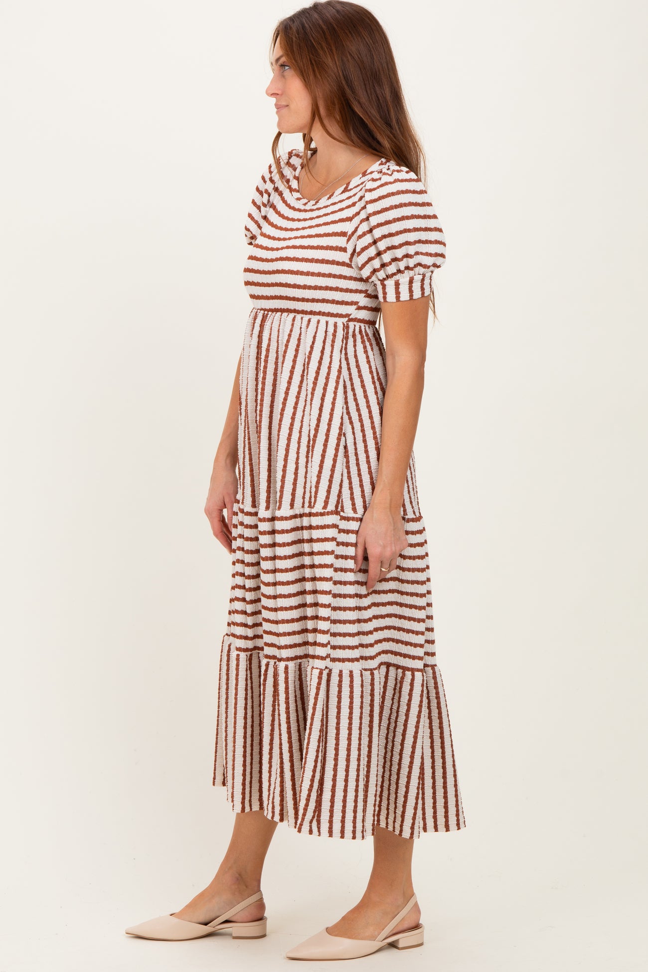 woman wearing a striped maxi dress with puff sleeves and a tiered skirt, paired with light-colored flat shoes